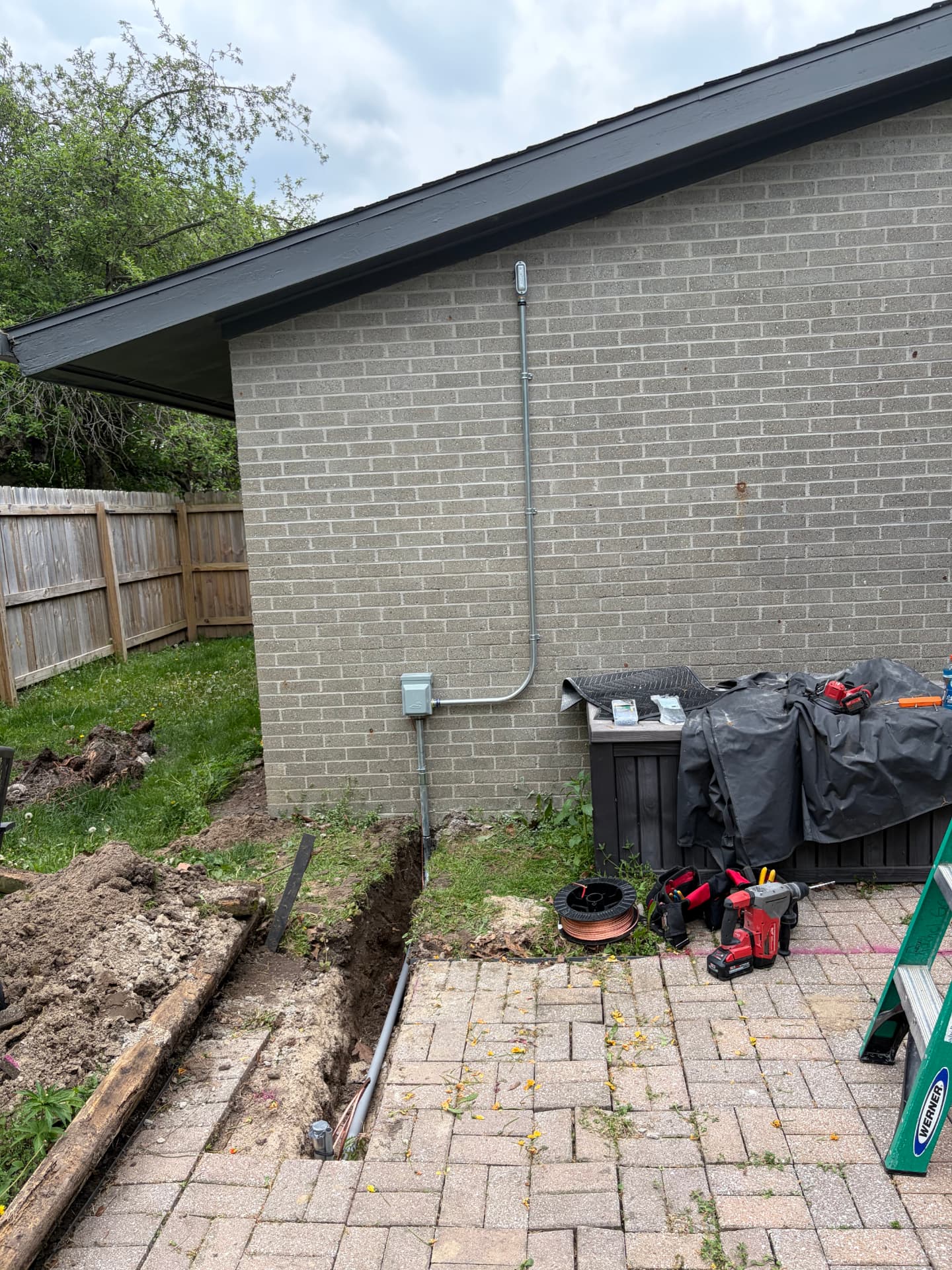 Trenched underground conduit feeding a new exterior circuit on a brick home